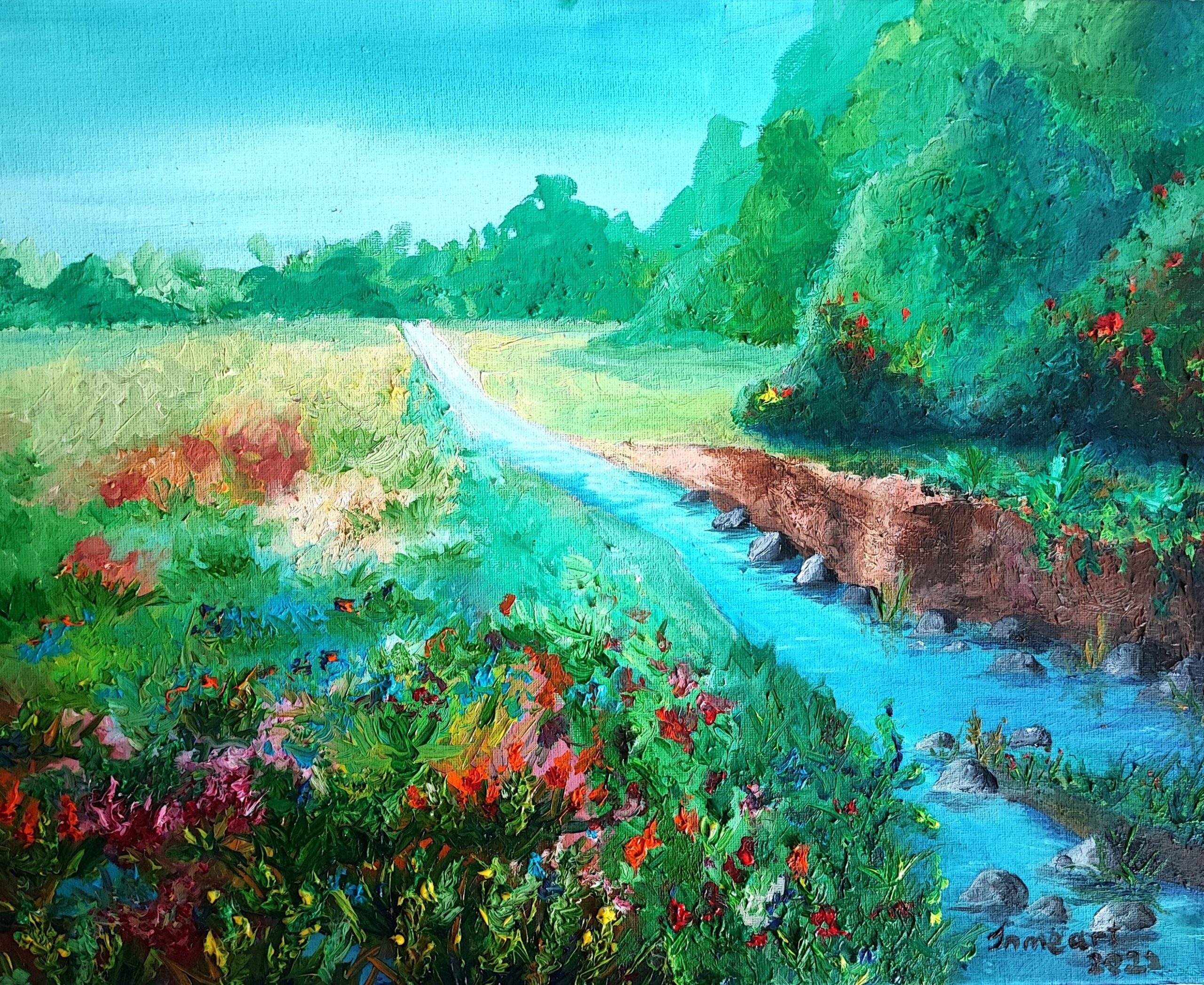 A bright, tranquil landscape showing a grassy path stretching into the distance beneath a blue sky. A stream runs alongside the path, bordered by vibrant wildflowers and dense green foliage. The right bank is slightly eroded, revealing earthy tones, while the left side bursts with reds, pinks, and purples from blooming flowers. The background features rolling green trees and bushes. The painting is signed 'in me art 2023' in the bottom right corner