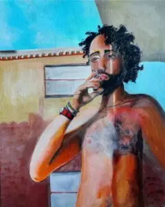 A realistic oil painting of a shirtless man with curly dark hair and a beard, standing under a bright blue sky near a stucco building. He is holding a cigarette to his lips, wearing a red wristwatch and colorful bracelets on his left wrist. His face is partially shadowed by the roof above, creating a dramatic light effect on his skin. The expression is contemplative, and the background features sunlit architectural details with warm earth tones. The painting is signed “in me art 2023” in the bottom right corner.
